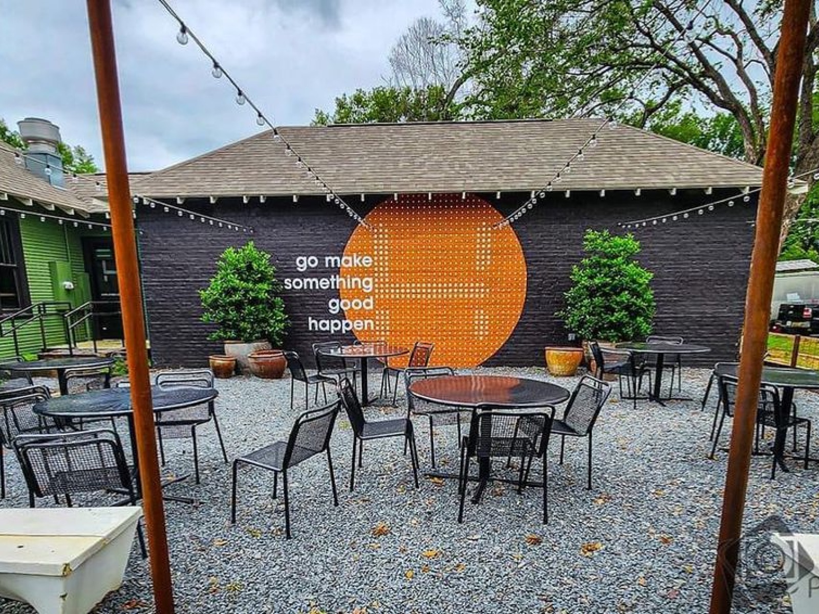 Local Habit’s patio: tables in front of a black brick wall with an orange circle mural reading “go make something good happen”